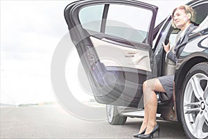 Mature businesswoman disembarking car with yellow lens flare in background