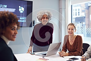 Mature Businesswoman Leading Creative Meeting Of Women Collaborating Around Table In Modern Office