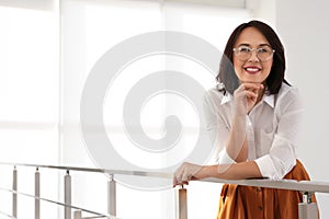 Happy mature businesswoman leaning on railing in office. Space for text