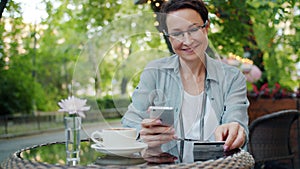 Mature businesswoman making payment with credit card using smartphone in cafe