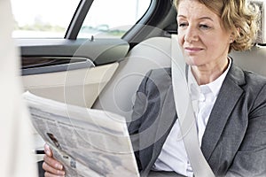 Mature businesswoman reading newspaper while sitting in car