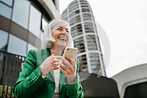 Mature businesswoman scrolling on smartphone, going home from work. Beautiful older woman with gray hair standing on