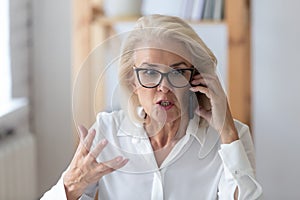 Mature businesswoman talking by phone arguing with client feels irritated