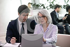 Mature businesswoman use laptop discussing business plan with younger colleague