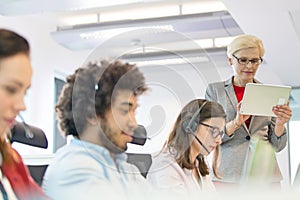 Mature businesswoman using digital tablet while operators working in office