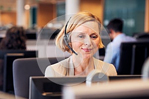 Mature Businesswoman Wearing Telephone Headset Talking To Caller In Customer Services Department