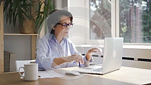 Mature businesswoman is working with laptop sitting in home office space.