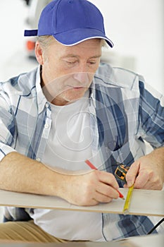 mature cabinet-maker measuring wooden plank using tape-line