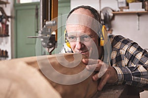 A mature carpenter cutting a piece of wood on a bandsaw