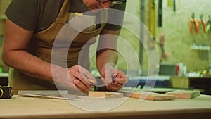 A mature carpenter makes works in his carpentry workshop, measures the wood by molting