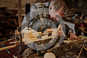 A mature carpenter works on a wooden toy sailboat in his workshop. Craftsman makes handmade wooden items