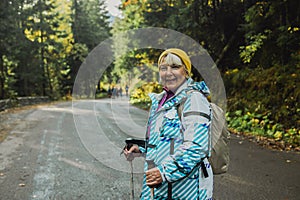 Mature caucasian blonde woman on vacation, having a hike in autumn mountains with backpack and hiking poles, enjoying