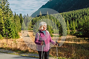 Mature caucasian blonde woman on vacation, having a hike in autumn mountains with backpack and hiking poles, enjoying