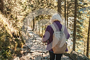 Mature caucasian blonde woman on vacation, having a hike in autumn mountains with backpack and hiking poles, enjoying