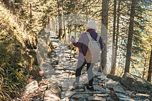 Mature caucasian blonde woman on vacation, having a hike in autumn mountains with backpack and hiking poles, enjoying