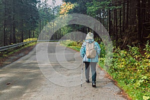 Mature caucasian blonde woman on vacation, having a hike in autumn mountains with backpack and hiking poles, enjoying