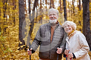 Mature caucasian couple with nordic sticks walking in autumn park, enjoying the weather