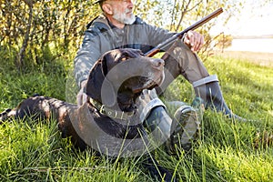 Mature caucasian hunter sitting with dog on grass