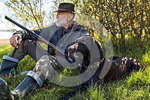 Mature caucasian hunter sitting with dog on grass