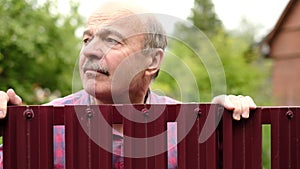 Mature caucasian man carefully watching over the fence. Curious neighbors and private life