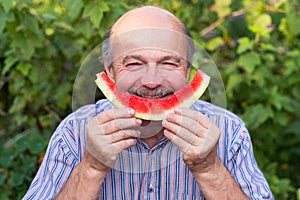 Mature caucasian man with mustache eating juicy water melon with pleasure and smiling.