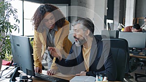 Mature Caucasian man and young Afro-American woman colleagues talking looking at computer screen