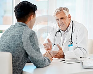 Mature caucasian medical doctor sitting with his patient during a consultation in a clinic and talking. Healthcare