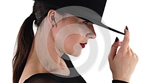 Mature charming woman posing with black hat on white studio background. Femme fatale, stylish outfit, pretty make-up.