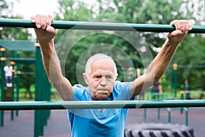 Mature cheerful pensioner man doing physical exercises on sports equipped playground