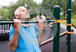 mature cheerful pensioner man doing physical exercises on sports equipped playground