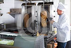 mature chef slicing kebab in fast food.