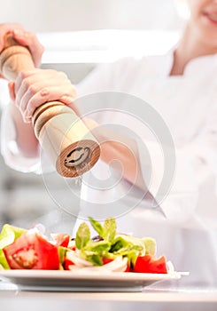 Mature chef using peppermill on salad in plate at restaurant with yellow lens flare in background