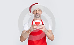 mature christmas man in red santa hat and apron holding coffee cup