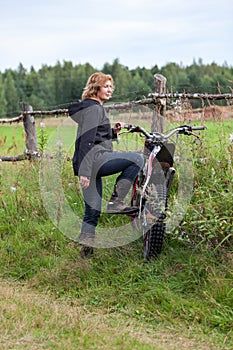 Mature countrywoman standing with dirt motorcycle on rural road
