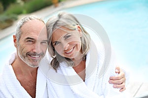 Mature couple with bathrobe sitting near pool