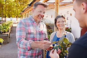 Mature Couple Buying Plants From Male Sales Assistant In Garden Center