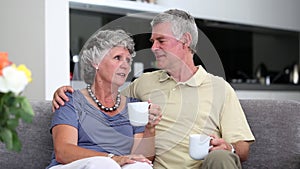 Mature couple chatting together with a cup of coffee on a sofa