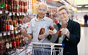 Mature couple chooses out salami in meat section of supermarket