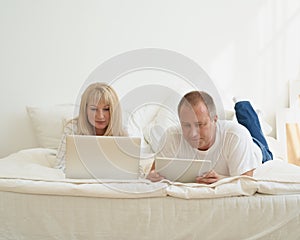 Mature couple with digital addiction at home. Man with tablet and woman with laptop