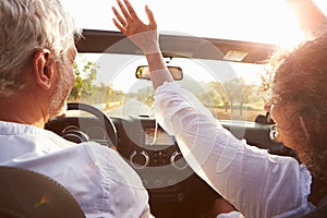 Mature Couple Driving Along Country Road In Open Top Car