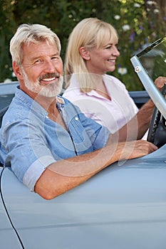 Mature Couple Enjoying Road Trip In Classic Open Top Sports Car Together