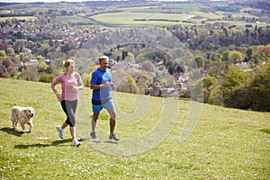 Mature Couple With Golden Retriever Jogging In Countryside