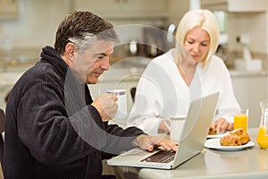 Mature couple having breakfast together man using laptop