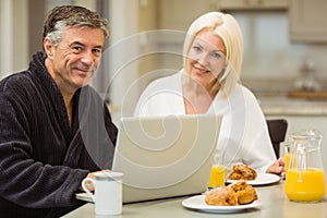 Mature couple having breakfast together man using laptop