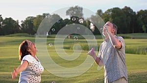 Mature couple having fun with bubble blowers outdoors.