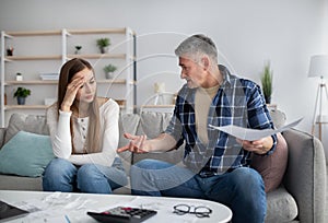 Mature couple having heated discussion about family budget, in trouble paying all bills, checking financial documents