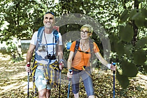 Mature couple hiking in forest wearing backpacks and hiking poles. Nordic walking, trekking. Healthy lifestyle