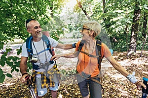Mature couple hiking in forest wearing backpacks and hiking poles. Nordic walking, trekking. Healthy lifestyle