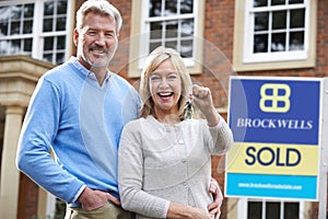 Mature Couple Holding Keys To New Home Standing By Sold Sign