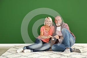 Mature couple with key sitting on floor in empty room. Moving into new house